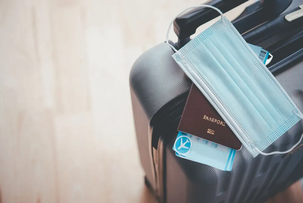 Luggage with passport, boarding passes, and face mask on top